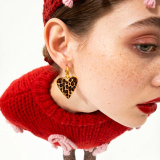 Close-up of a person wearing a gold heart-shaped earring with leopard print details, against a white background.